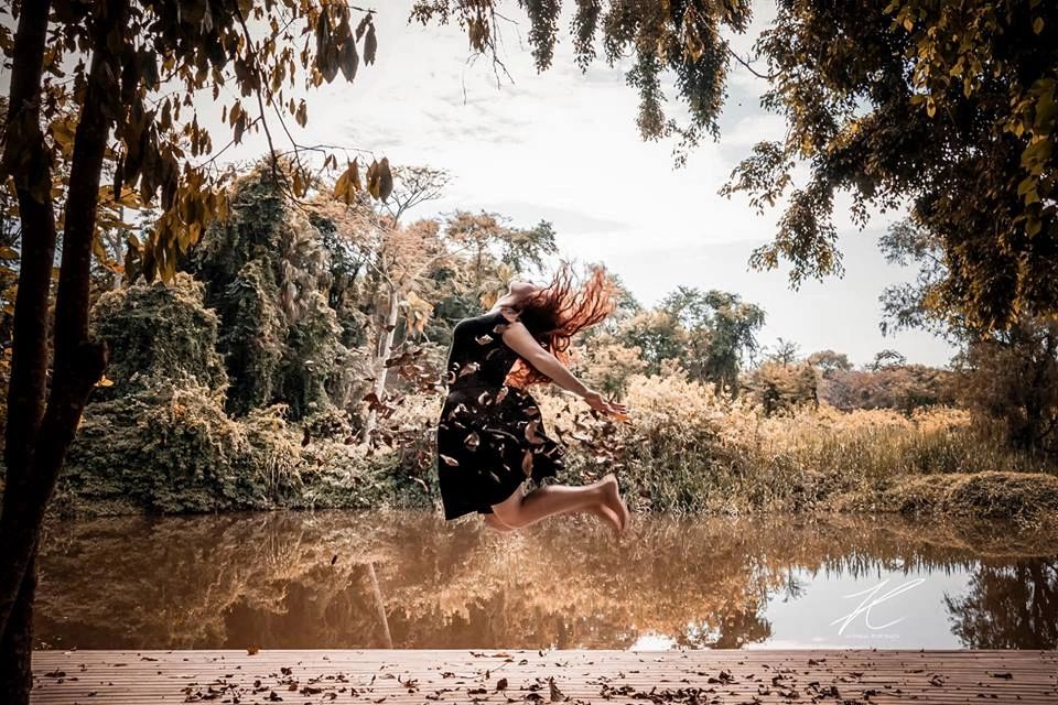 Model leaping above a lake surrounded by autumn leaves